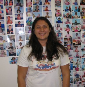 Aquatics Manager Stephanie Bachar stands in front of the wall of British Swim School student photos